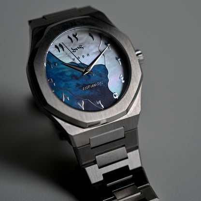 Montre automatique Arabic Dial pour homme avec chiffre arabe et cadran bleu vu de face et posé au sol.